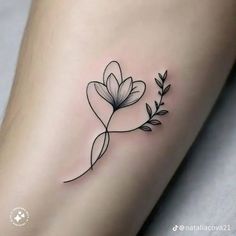 a small flower tattoo on the side of a woman's leg, with leaves around it