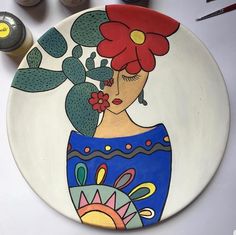 a plate with a woman's face painted on it next to paintbrushes