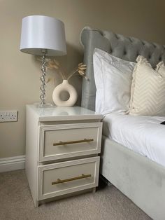 a nightstand with two drawers and a lamp on top of it next to a bed