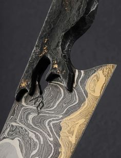 a close up of a knife on a black surface with gold and white swirls