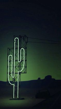 a large neon cactus sitting on top of a tall metal structure in the middle of a field