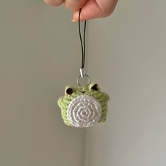 a crocheted frog ornament hanging from a string in someone's hand