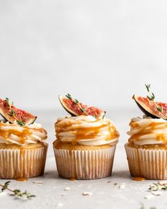 three cupcakes with white frosting and topped with figurines, garnished with fresh herbs