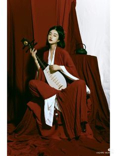 a woman sitting on a chair with a guitar in her hand and red curtains behind her