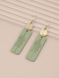 pair of green earrings with gold disc and palm tree design on the front, hanging from hooks