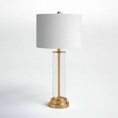 a lamp with a white shade on the top and a gold base, sitting in front of a white background