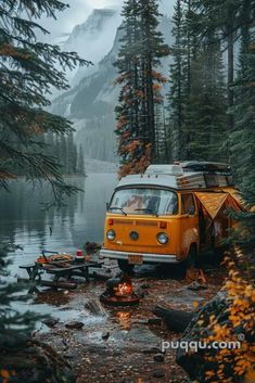 an orange camper van parked next to a lake in the woods with trees around it