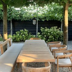 a wooden table surrounded by white chairs under a pergolated roof with trees in the background