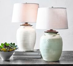 two white vases sitting on top of a wooden table next to a potted plant