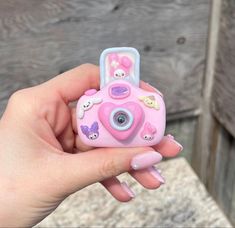 a hand holding a pink camera with stickers on it