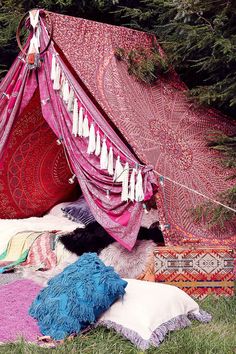 a tent that is covered in blankets and tassels on the ground next to some trees