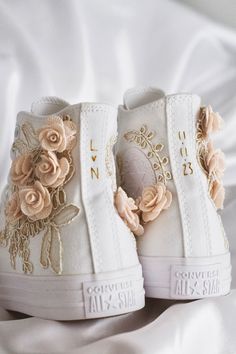 a pair of white high top sneakers with flowers on the side and gold trimmings