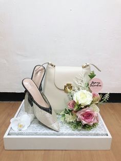 a white purse and shoes on display in a box next to a bouquet of flowers