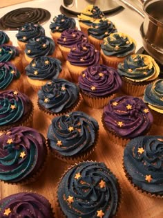 cupcakes with blue and purple frosting are arranged on a wooden board next to a stove