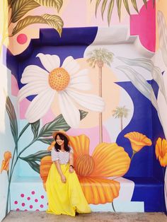 a woman sitting on a bench in front of a colorful wall with flowers and palm trees