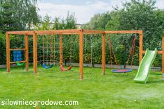 a wooden swing set with swings and a green slide in the grass next to some trees