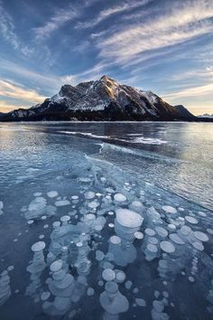 ice floes are floating on the water in front of a mountain and blue sky