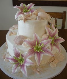 a wedding cake with pink flowers and seashells on top