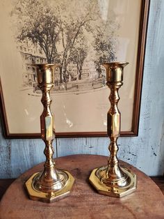 two golden candlesticks sitting on top of a wooden table next to a painting