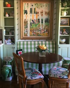 two chairs and a table in a room with paintings on the wall behind them,