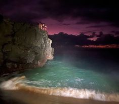 a person laying on top of a cliff next to the ocean under a purple sky