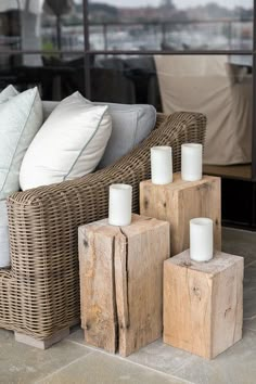 candles are placed on wooden blocks in front of a wicker couch with cushions and pillows