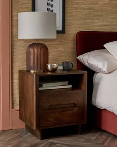 a nightstand with a lamp on top of it next to a bed