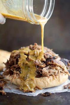 someone pouring sauce onto a pulled pork sandwich