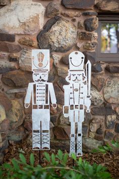 two paper cut out figures standing in front of a stone wall with plants and rocks