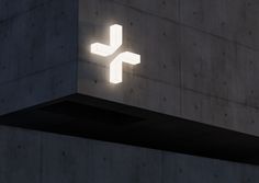 a lit up cross on the side of a building in front of a concrete wall