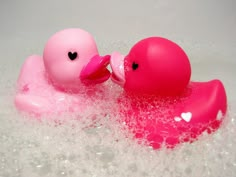 two rubber ducks are in the bathtub with bubbles on it's sides and one is pink