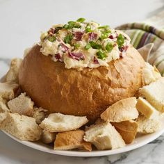 a white plate topped with a large bowl filled with food next to crackers and chips