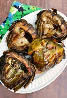 grilled artichokes on a white plate sitting on a wooden table next to a napkin