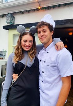 a man standing next to a woman in front of a building with mickey ears on his head