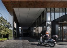 a man riding a motorcycle down a street next to a tall building with lots of windows