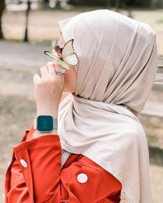 a woman wearing a hijab and holding a butterfly in her hand while sitting on a bench