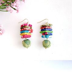 two pairs of earrings with colorful beads hanging from them next to pink flowers on a white surface