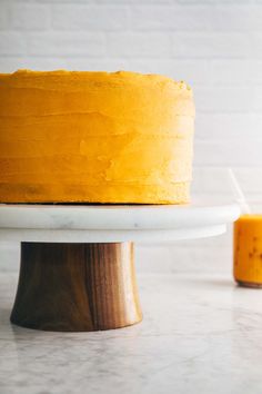 a yellow cake sitting on top of a white cake plate next to a small candle