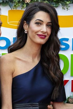 a woman with long dark hair wearing a one shoulder dress and smiling at the camera