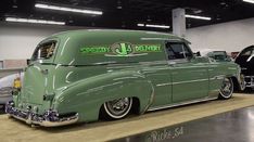 an old green car is parked in a showroom with other classic cars behind it