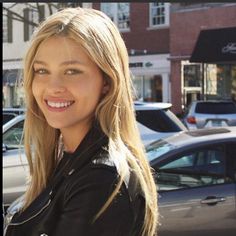 a woman standing in front of parked cars on a city street with her arms crossed