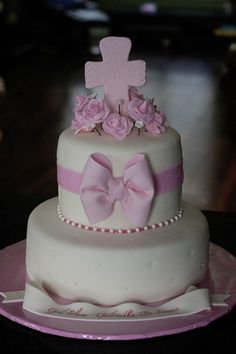 a three tiered cake decorated with pink flowers and a cross on the top layer