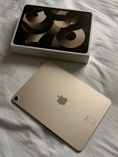 an apple laptop sitting on top of a bed next to a box with the lid open