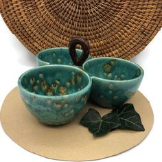 three blue bowls sitting on top of a table next to a wicker basket and ivy