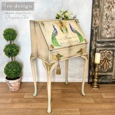 an ornate white piano with peacocks painted on the front and sides, next to a potted plant