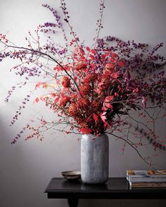 a vase filled with red and purple flowers on top of a wooden table next to books