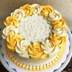 a cake with yellow and white frosting roses on it sitting on a platter