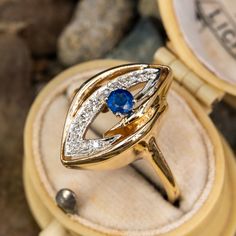 This fun vintage sapphire ring is in the shape of a navette and features an open center that is set with a white gold and diamond element as well as a bright blue round sapphire. The ring has milgrain detailing and it is crafted in 14k yellow gold. One of the diamonds has a small chip but nothing distracting. Vintage Blue Sapphire Ring With Diamond Accents, Vintage Blue Sapphire Ring With Bezel Setting, Vintage Marquise Sapphire Ring For Formal Occasions, Vintage Blue Marquise Sapphire Ring, Vintage Sapphire Ring With Marquise Cut Diamond, Vintage Marquise Cut Sapphire Ring With Diamond, Vintage Marquise Cut Sapphire Ring Gift, Vintage Sapphire Ring, Round Sapphire