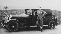 an old black and white photo of a man standing next to a car