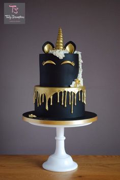 a black and gold cake decorated with an unicorn's face, horn, and dripping icing